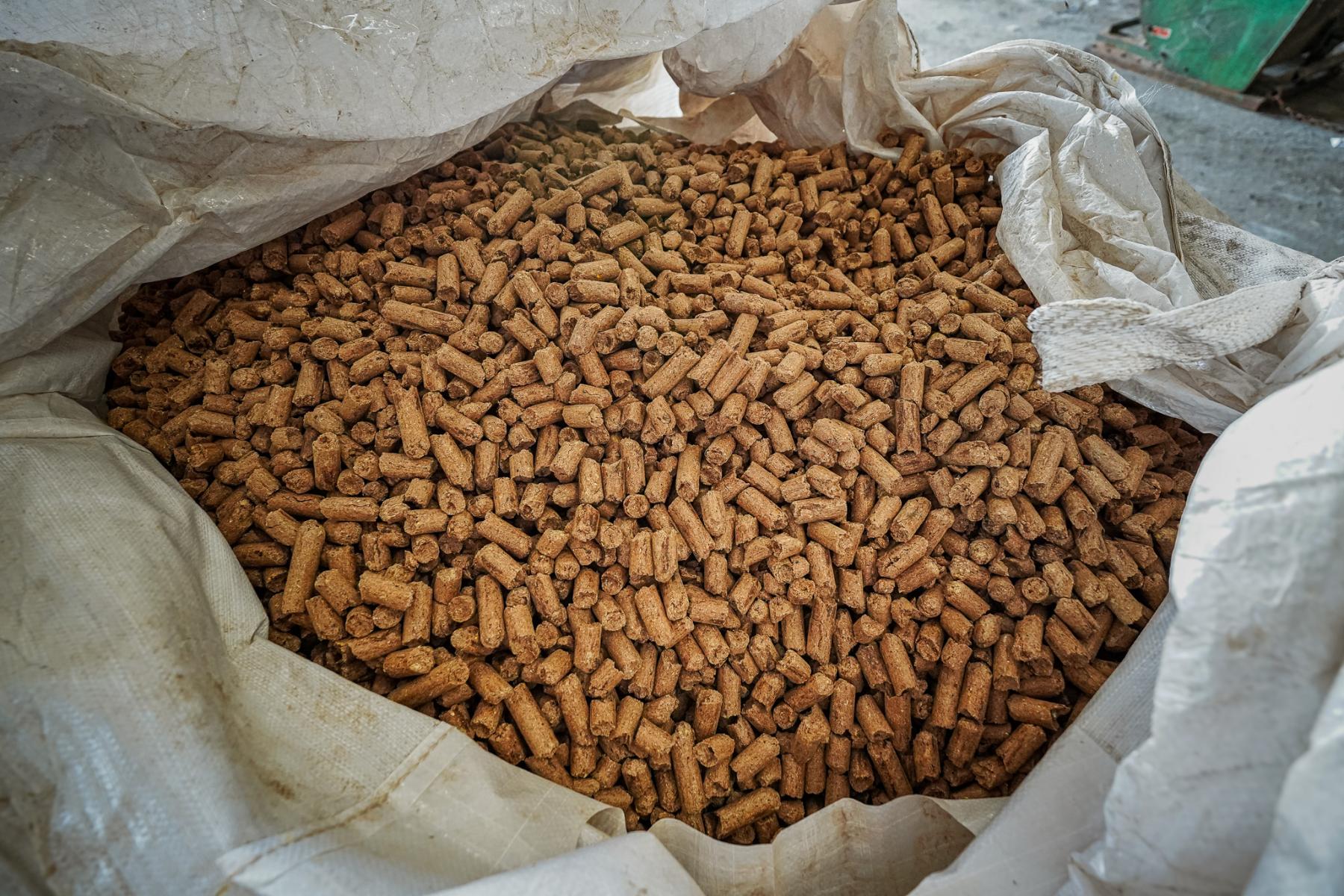 Close-up of molasses-based livestock feed pellets inside a large bulk tote bag at a feed manufacturing facility.